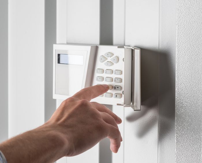person typing on keypad of home security alarm, security system concept
