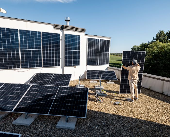 Man carries solar panel while installing solar plant of a rooftop of his property. Wide angle view. Renewable energy for self consumption concept. Idea of installing panels for households